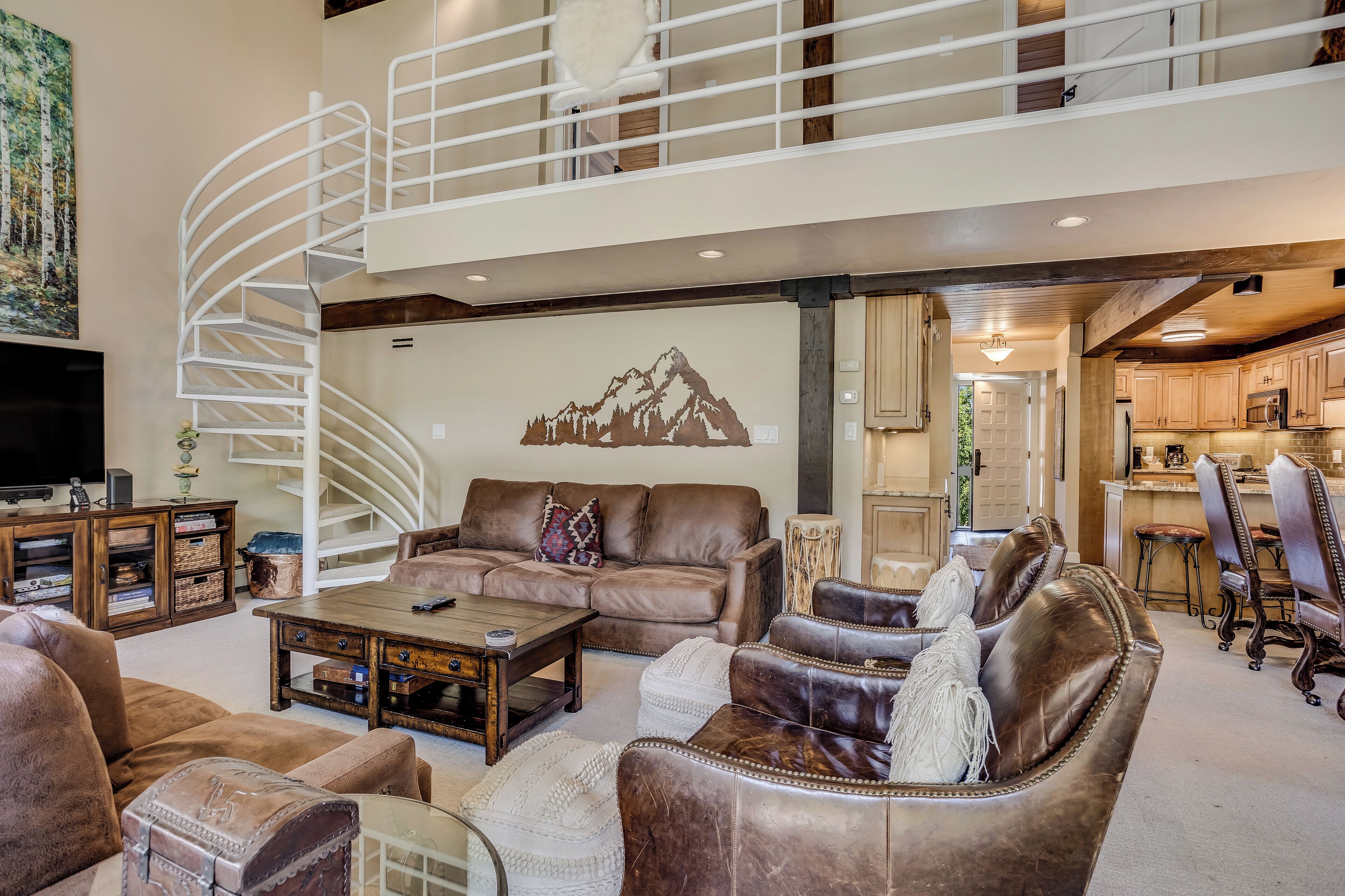 A spacious living area with a high ceiling, a spiral staircase, and a view into the kitchen.