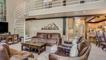 A spacious living area with a high ceiling, a spiral staircase, and a view into the kitchen.