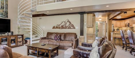 A spacious living area with a high ceiling, a spiral staircase, and a view into the kitchen.
