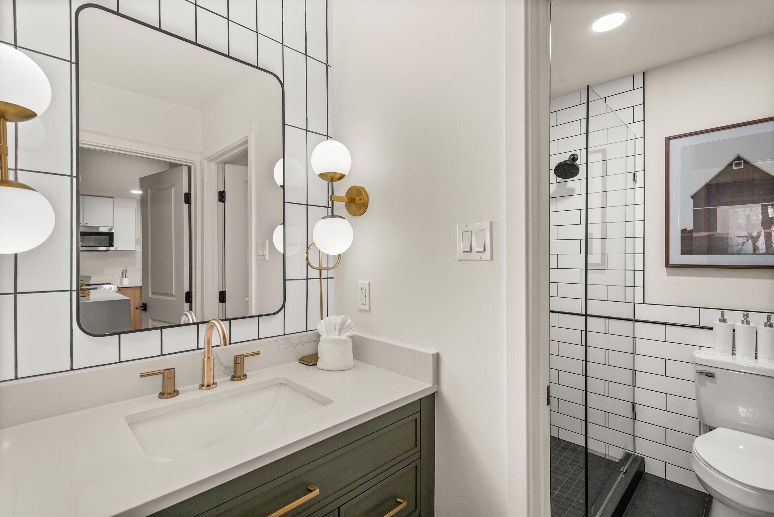 Een moderne badkamer met een wit wastafelmeubel, gouden kraanwerk en een grote spiegel met ronde verlichting.