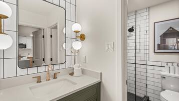 Een moderne badkamer met een wit wastafelmeubel, gouden kraanwerk en een grote spiegel met ronde verlichting.