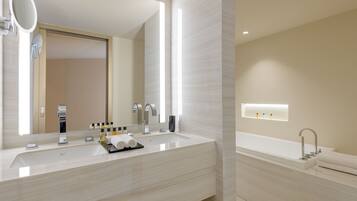 A modern bathroom with a large mirror, a sink with two faucets, and a bathtub.