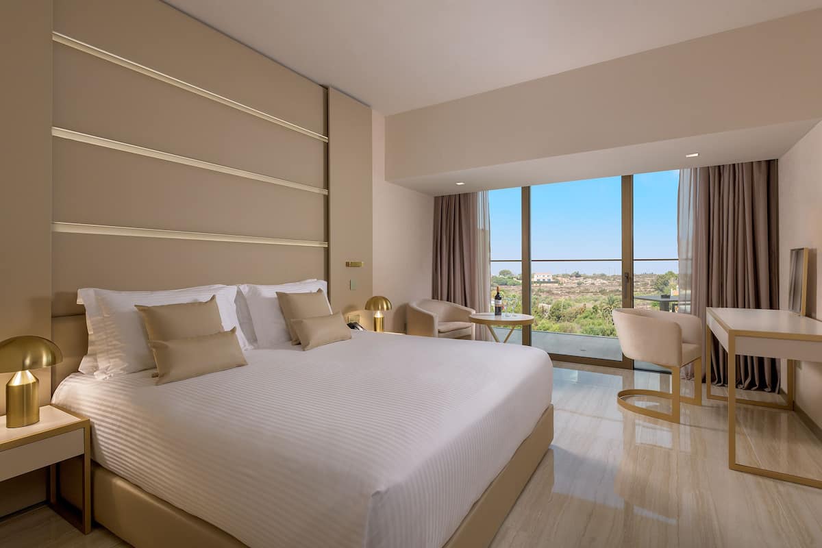 A modern hotel room with a large bed, a desk, and a view of the city.