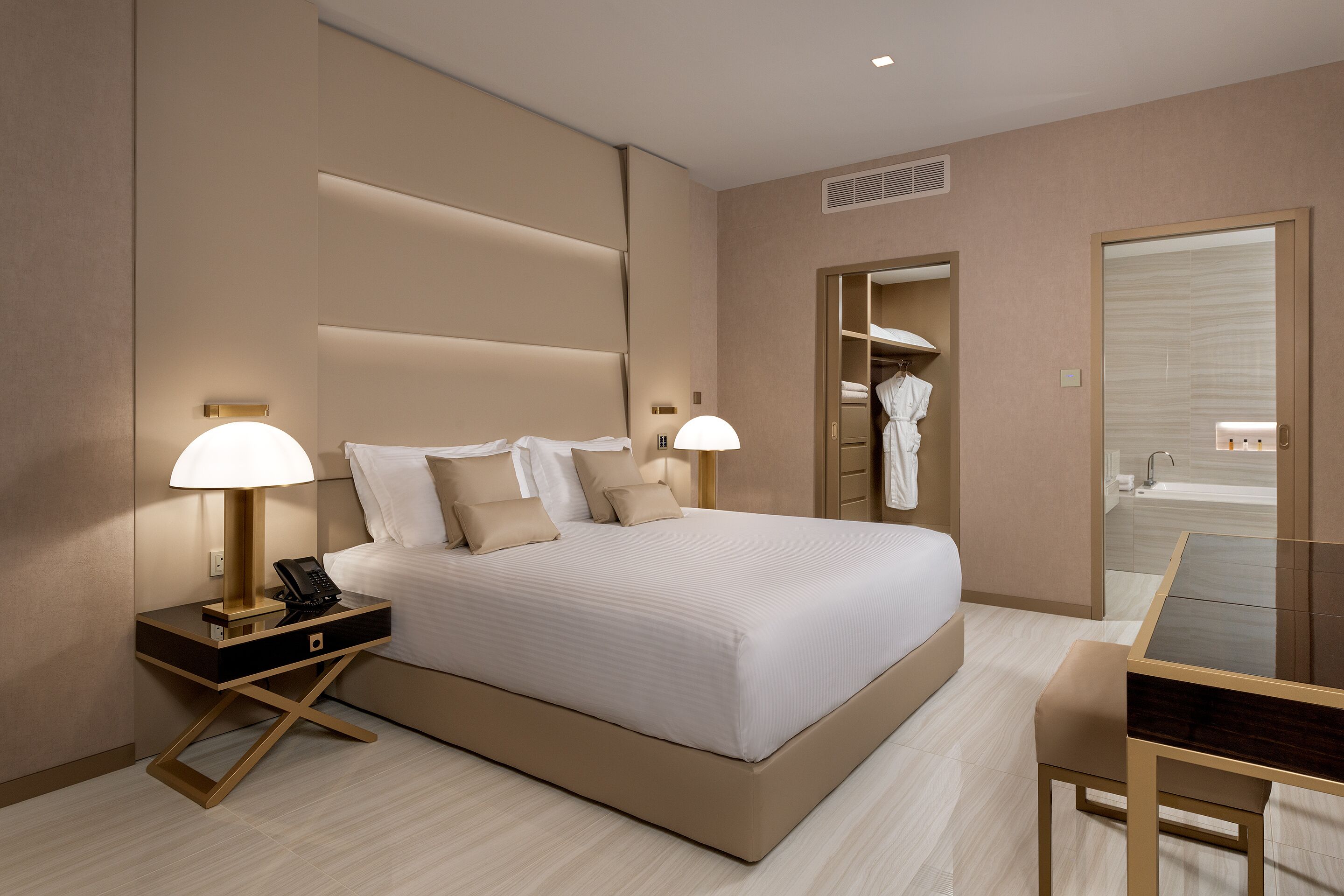 Una camera d'hotel moderna con un letto grande, lampade ai comodini, una scrivania e un armadio a muro.