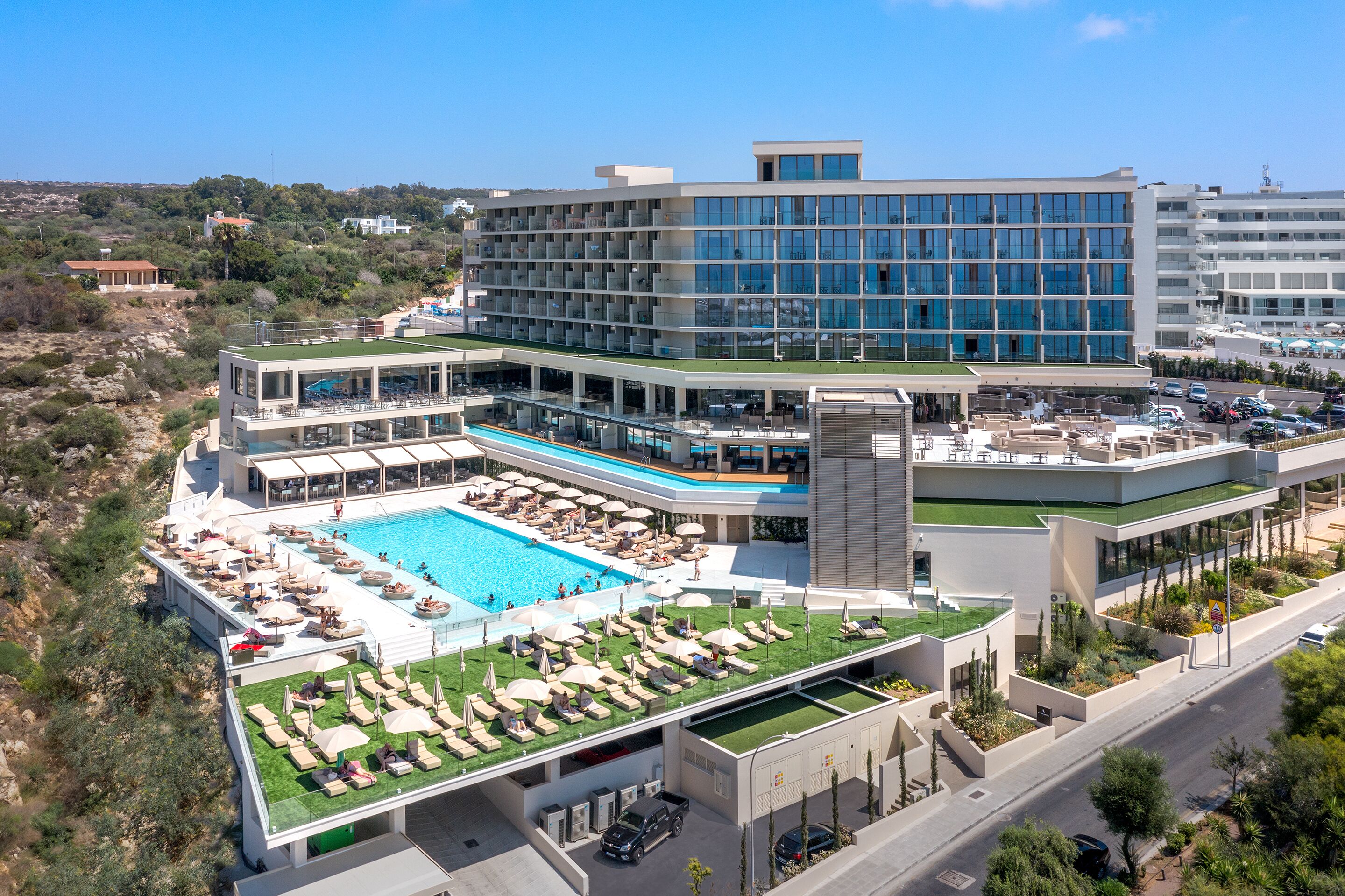 A modern hotel with a rooftop pool, multiple balconies, and a landscaped garden area.