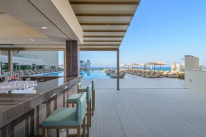 A rooftop bar with a pool view, bar area, and lounge chairs. - AMARANDE Adults Only (Ayia Napa)