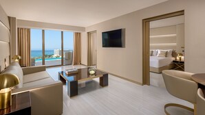 A modern hotel room with a large window, a flat-screen TV, a sofa, a coffee table, and a bed. - AMARANDE Adults Only (Ayia Napa)