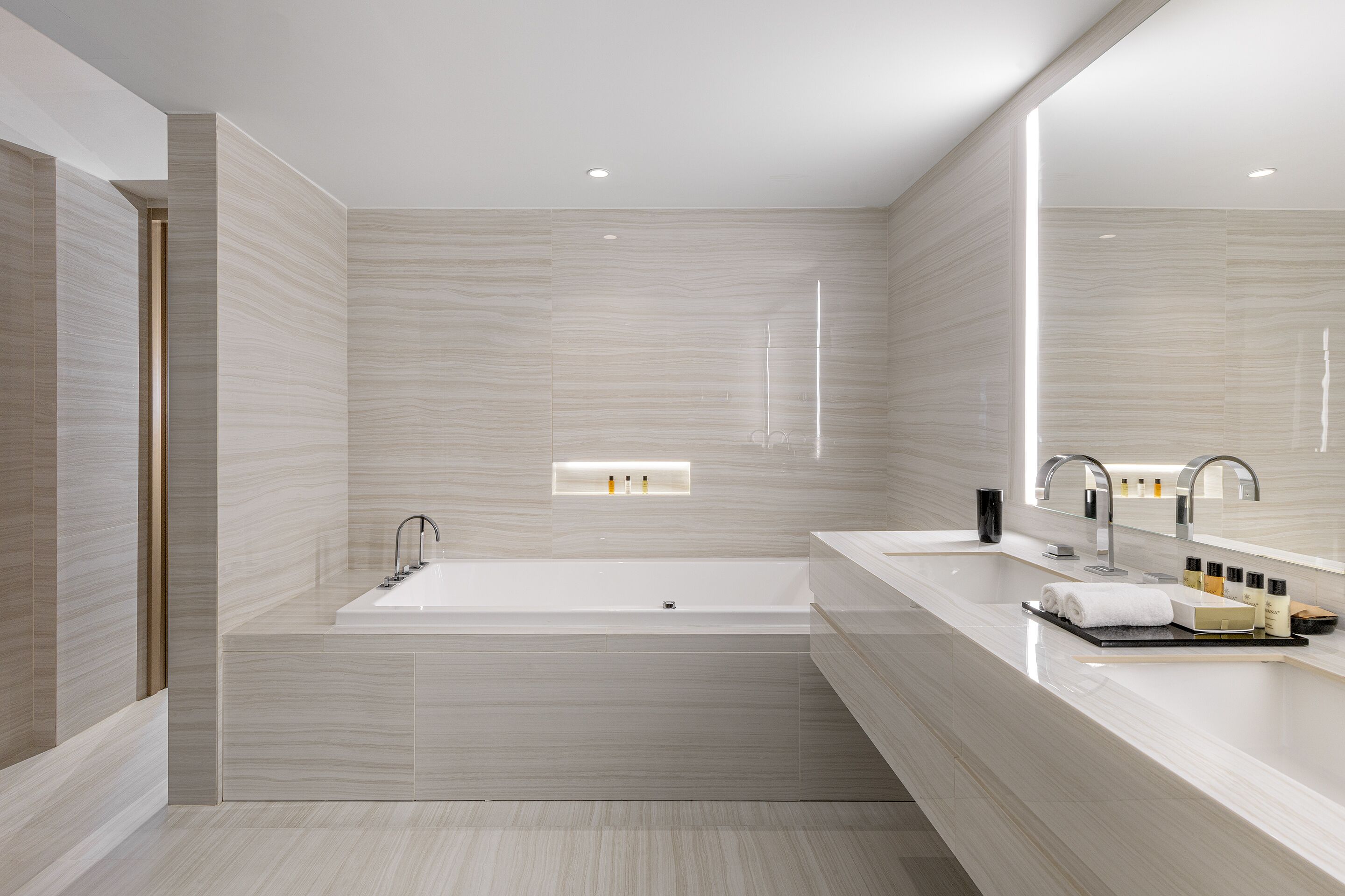 A modern bathroom with a large bathtub, two sinks, and a mirror.