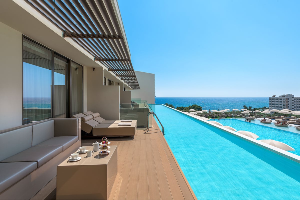 A modern outdoor pool area with a long, narrow pool, a seating area with a sofa and a table, and a view of the ocean.