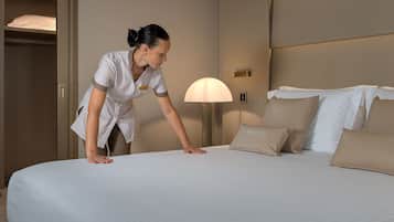 A neatly made bed with a white and beige color scheme, a bedside lamp, and a closed wardrobe.