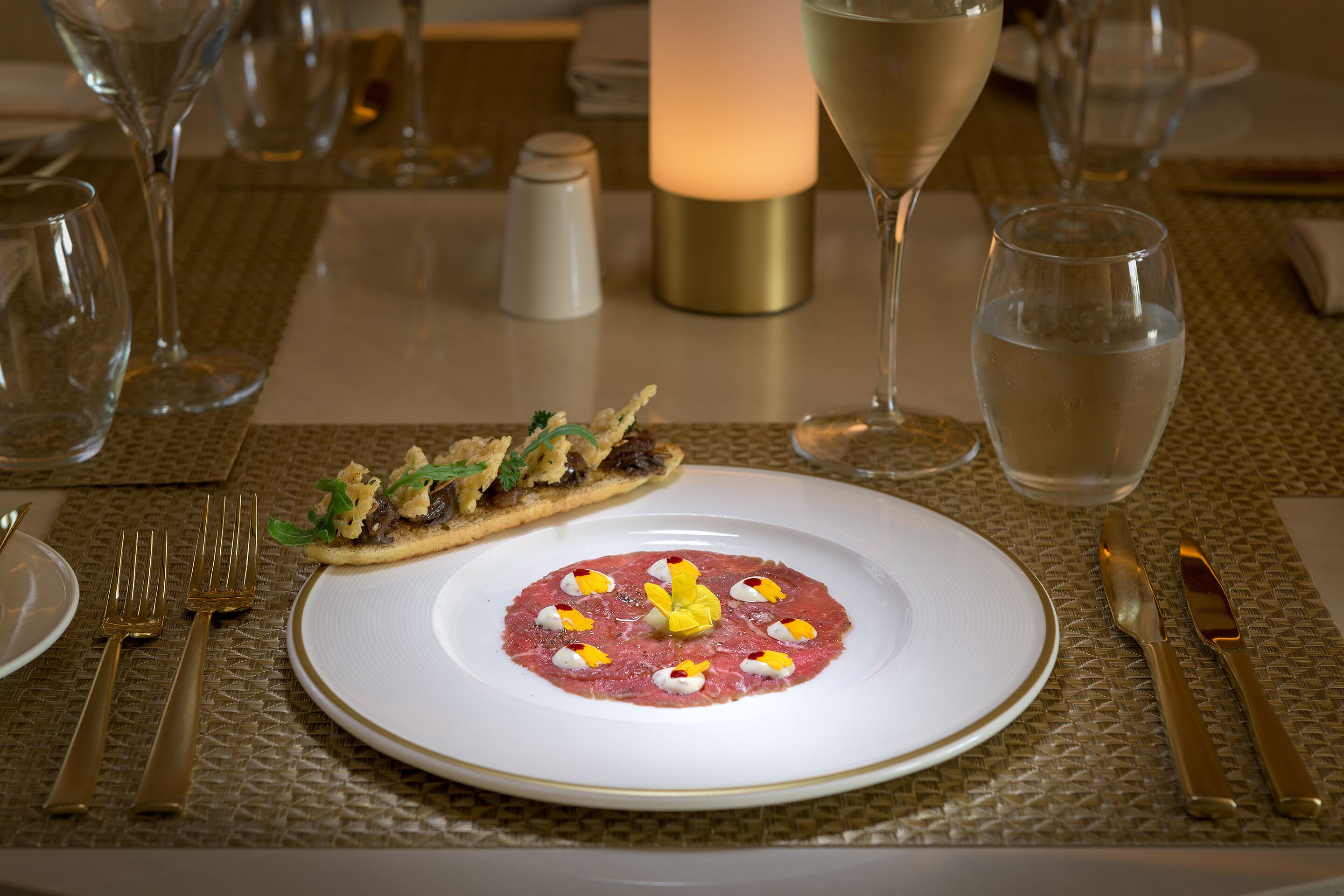 A dining table with a white plate of food, a glass of water, and a candle.