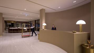 Un hall d’hôtel moderne avec un comptoir d’accueil, un homme qui marche et une femme assise.