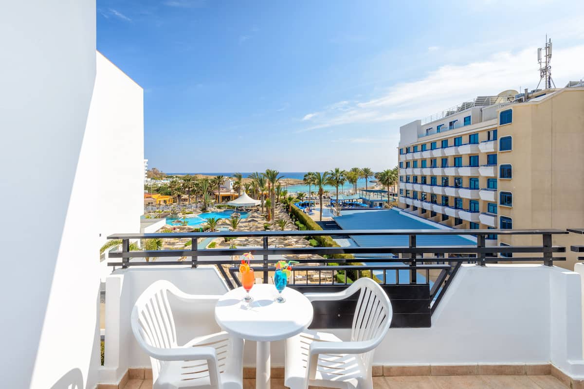Balcón con mesa y sillas con vista a una piscina y al área de un complejo turístico.