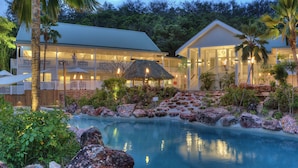 A resort with a swimming pool surrounded by rocks and tropical plants, featuring multiple-story buildings with balconies and a thatched-roof structure. - Malolo Island Resort (Malolo Island)