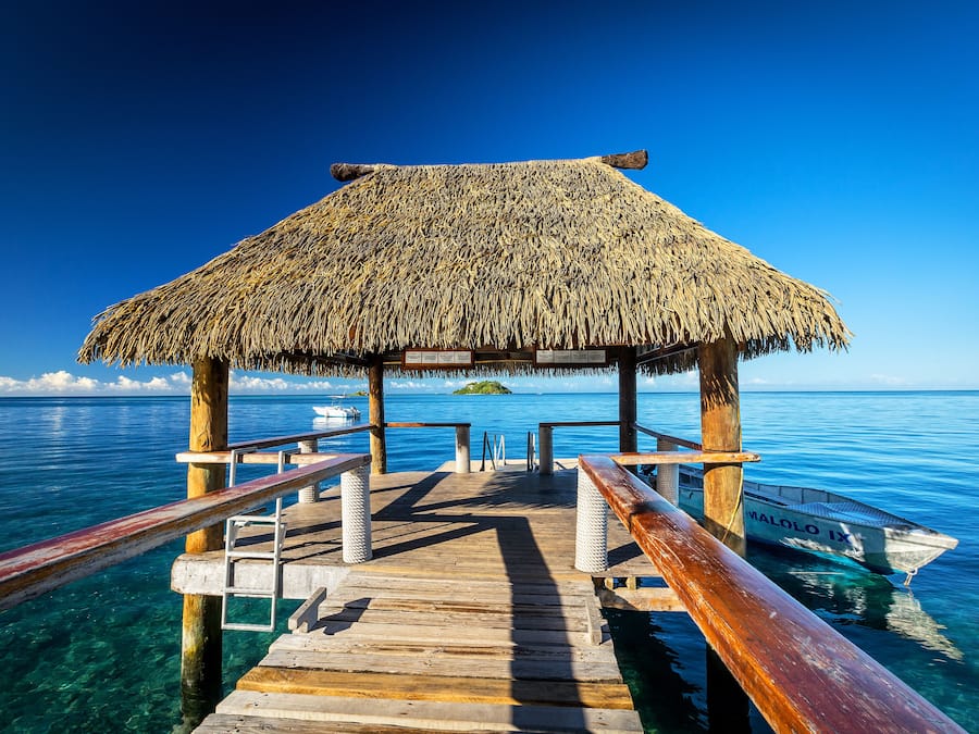 A wooden pier leading to a thatched-roof structure over clear blue water.