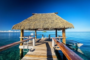 Un muelle de madera que conduce a una estructura de techo de paja sobre aguas azul cristalino.
