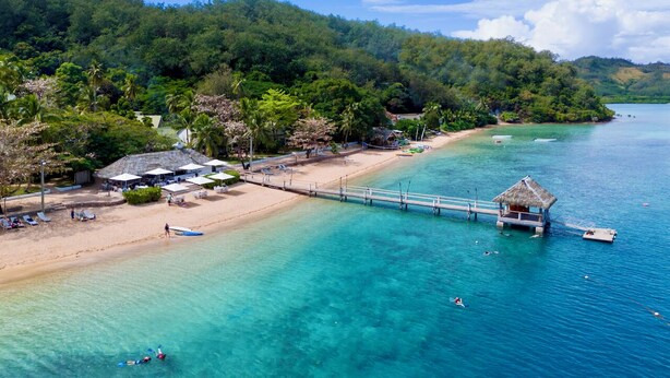 A beach with a pier, clear turquoise water, and lush greenery. - Malolo Island Resort (Malolo Island)