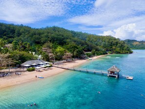 Una playa con muelle, agua turquesa cristalina y exuberante vegetación.