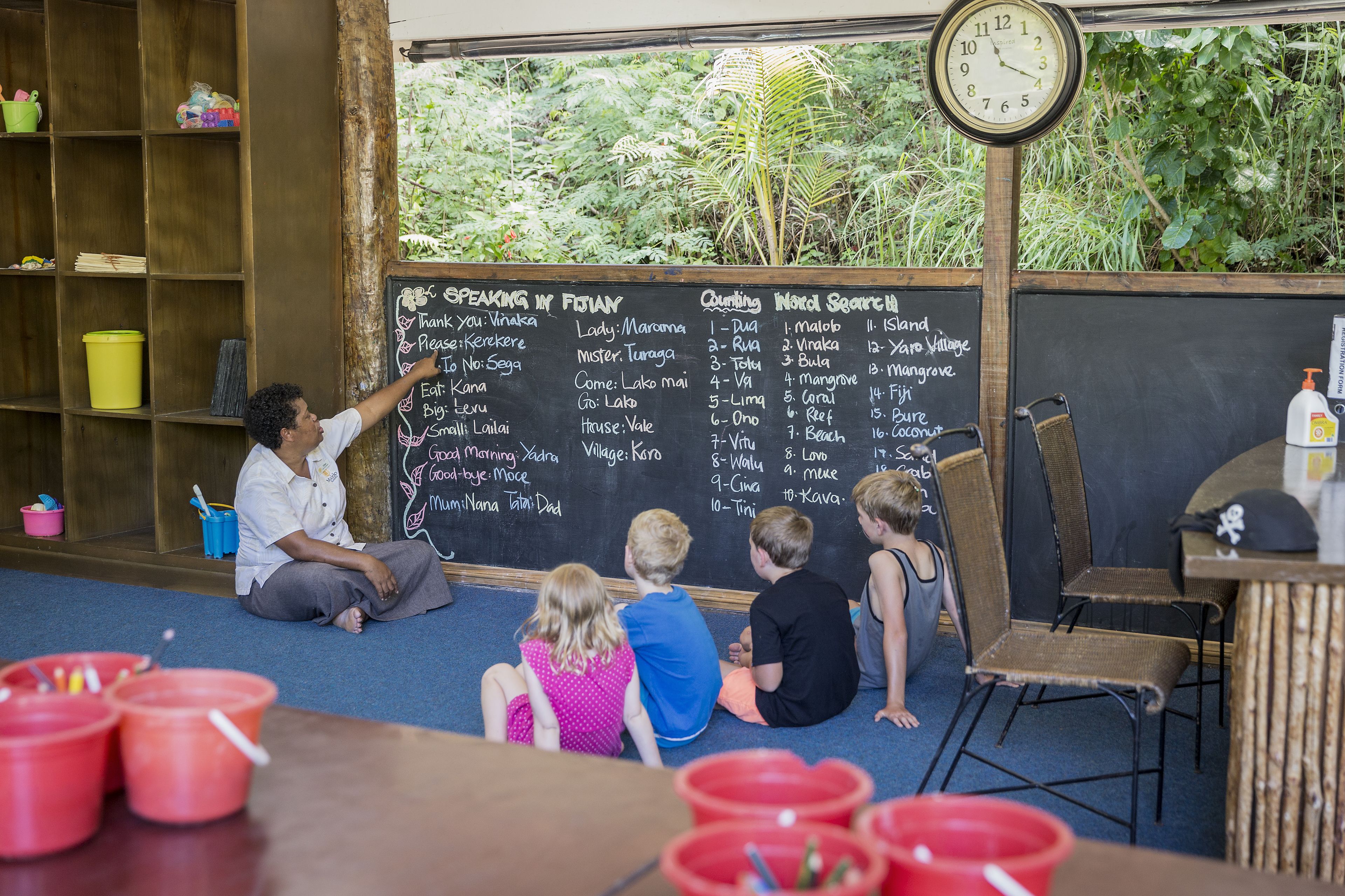 A classroom with a chalkboard listing names and a clock on the wall.