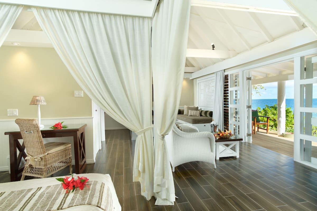 Una habitación con una cama, una silla de mimbre, una mesa de comedor y un frutero, y vista al océano.