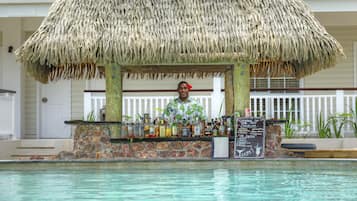 Un bar tiki con techo de paja, mostrador de piedra y una pizarra de menú.