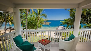 A balcony with white wicker furniture, a small table with a flower, and a view of the ocean and palm trees. - Malolo Island Resort (Malolo Island)