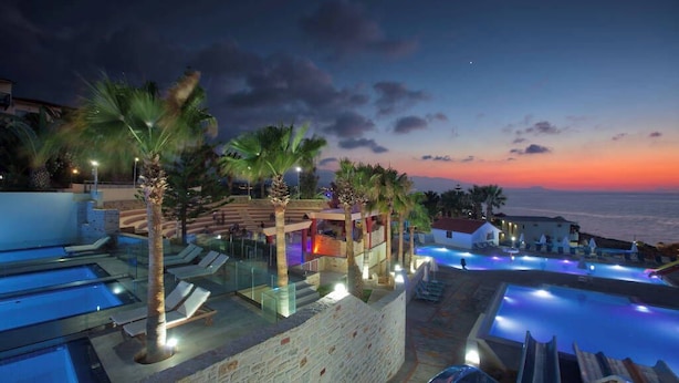 Un resort con varias piscinas, palmeras y vistas al atardecer.