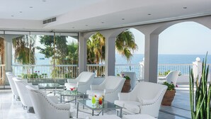 Amplio espacio interior con sillas de cuero blanco y una mesa de vidrio, con vistas a un balcón y al mar.