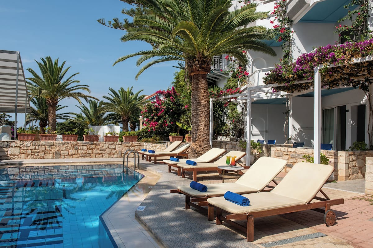A poolside area with lounge chairs, a palm tree, and a stone wall.
