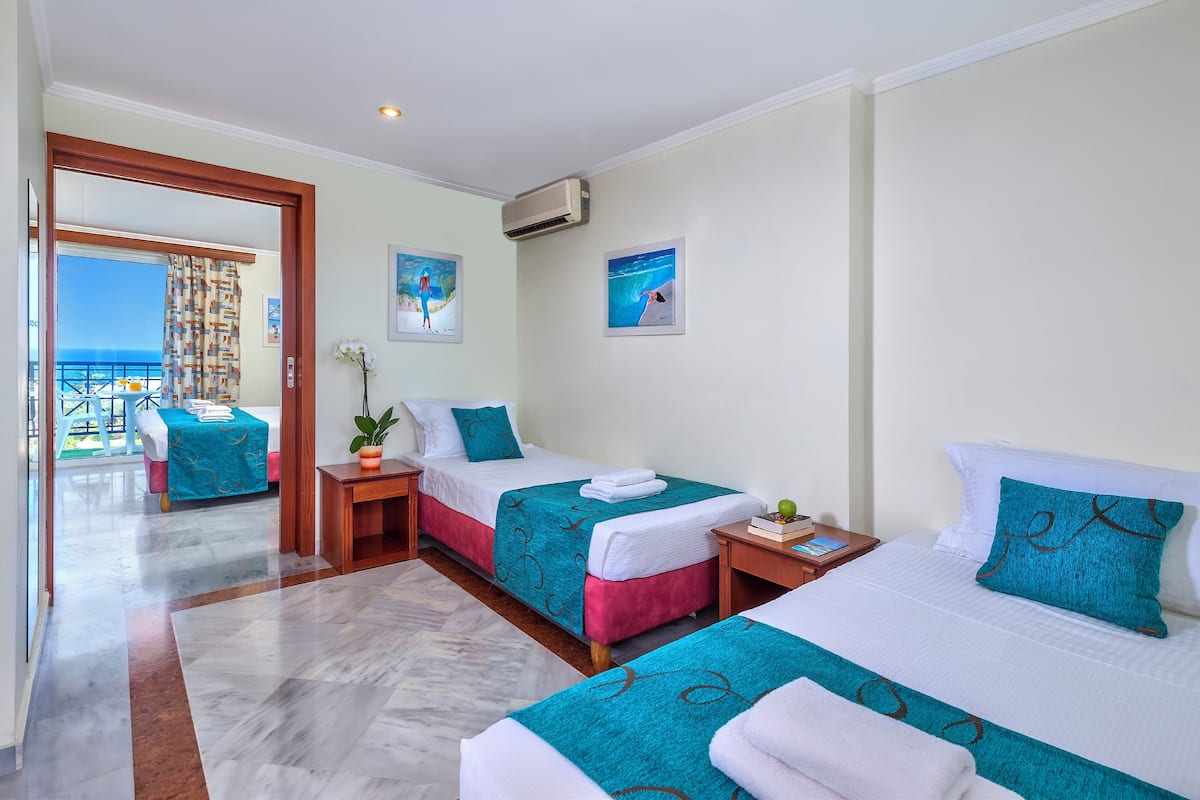A hotel room with two beds, a balcony with a view, and a small table with a plant.