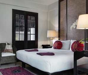 A hotel room with a large bed, a chair, a desk, a lamp, and a window. - Tamarind Village (Chiang Mai)