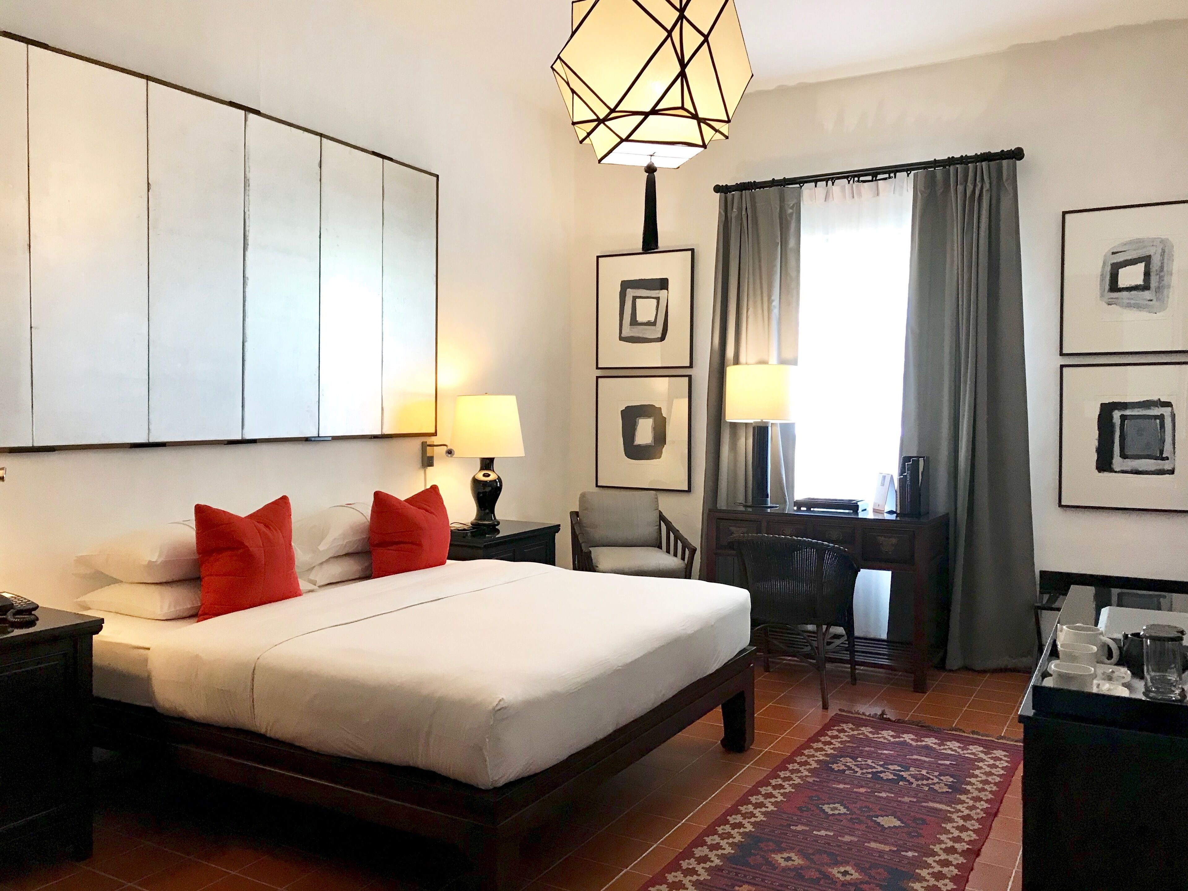 Habitación de hotel con una cama grande, dos mesitas de noche, un escritorio con una silla, un tapete estampado y obras de arte en las paredes.