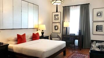 Habitación de hotel con una cama grande, dos mesitas de noche, un escritorio con una silla, un tapete estampado y obras de arte en las paredes.
