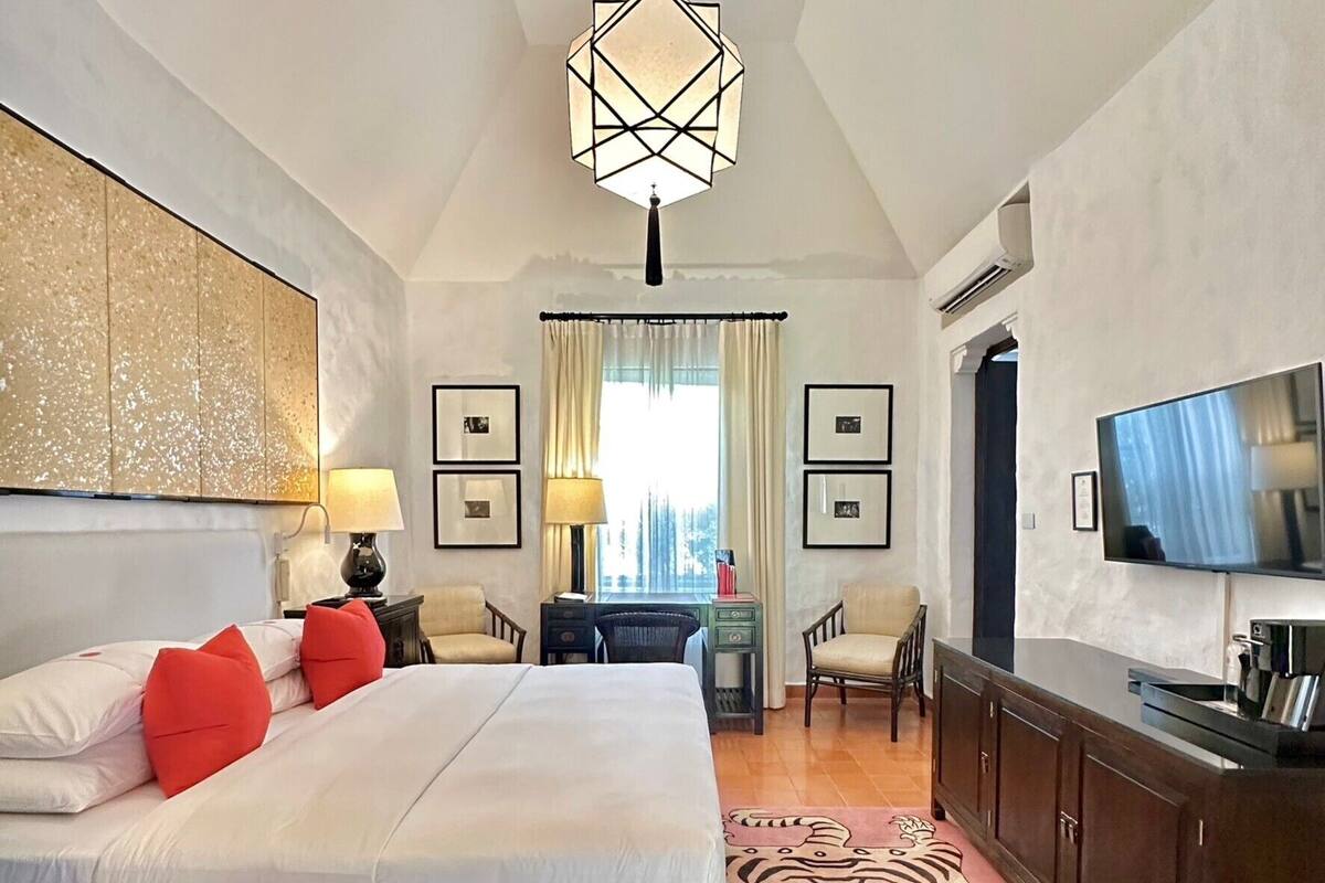 A hotel room with a large bed, a desk, a television, and a patterned rug.