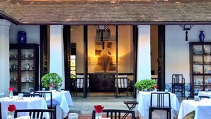An outdoor dining area with tables set for two, chairs, and a view into the restaurant interior. - Rachamankha Hotel (Chiang Mai)