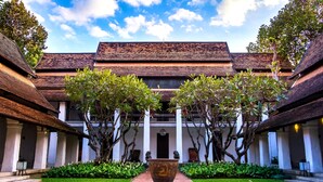 A courtyard with a central pathway, surrounded by trees and a large decorative urn. - Rachamankha Hotel (Chiang Mai)