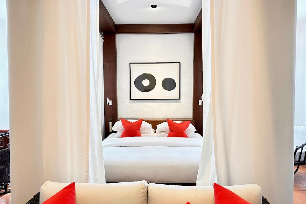 A hotel room with a bed, a framed artwork on the wall, and a view of the outside.