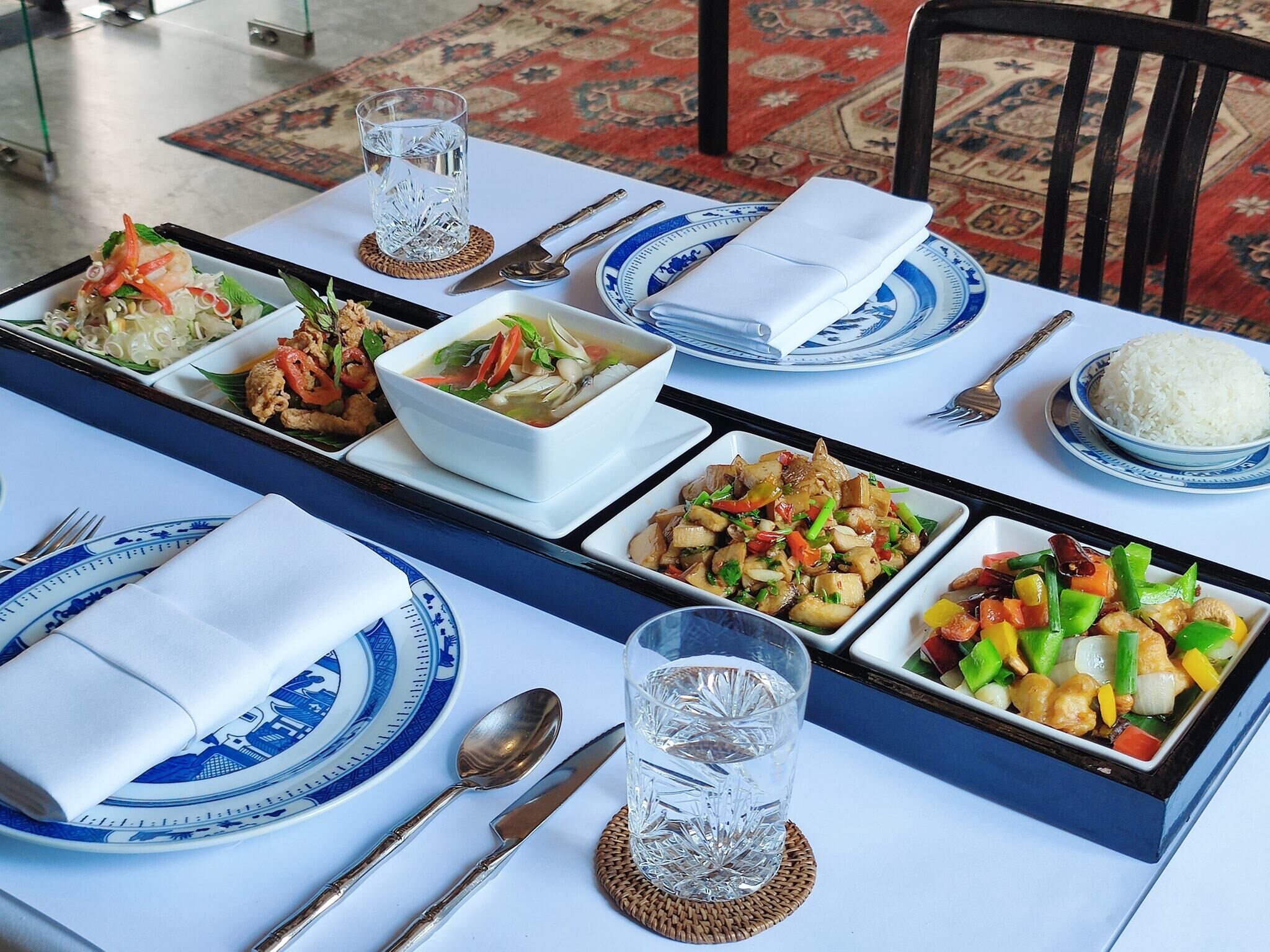 Una mesa de comedor dispuesta con diferentes platos, cubiertos y vasos.