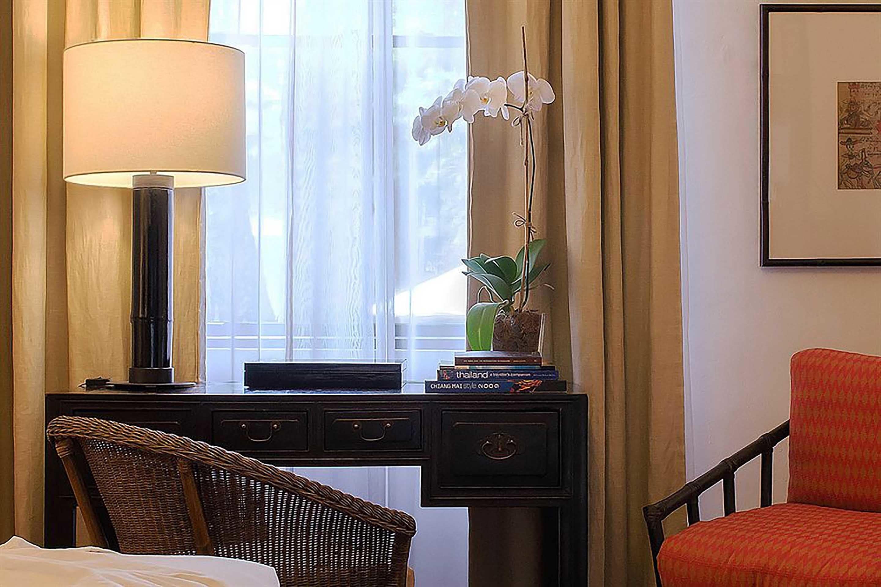 Habitación de hotel con escritorio, lámpara, orquídea en maceta, silla e imagen enmarcada en la pared.
