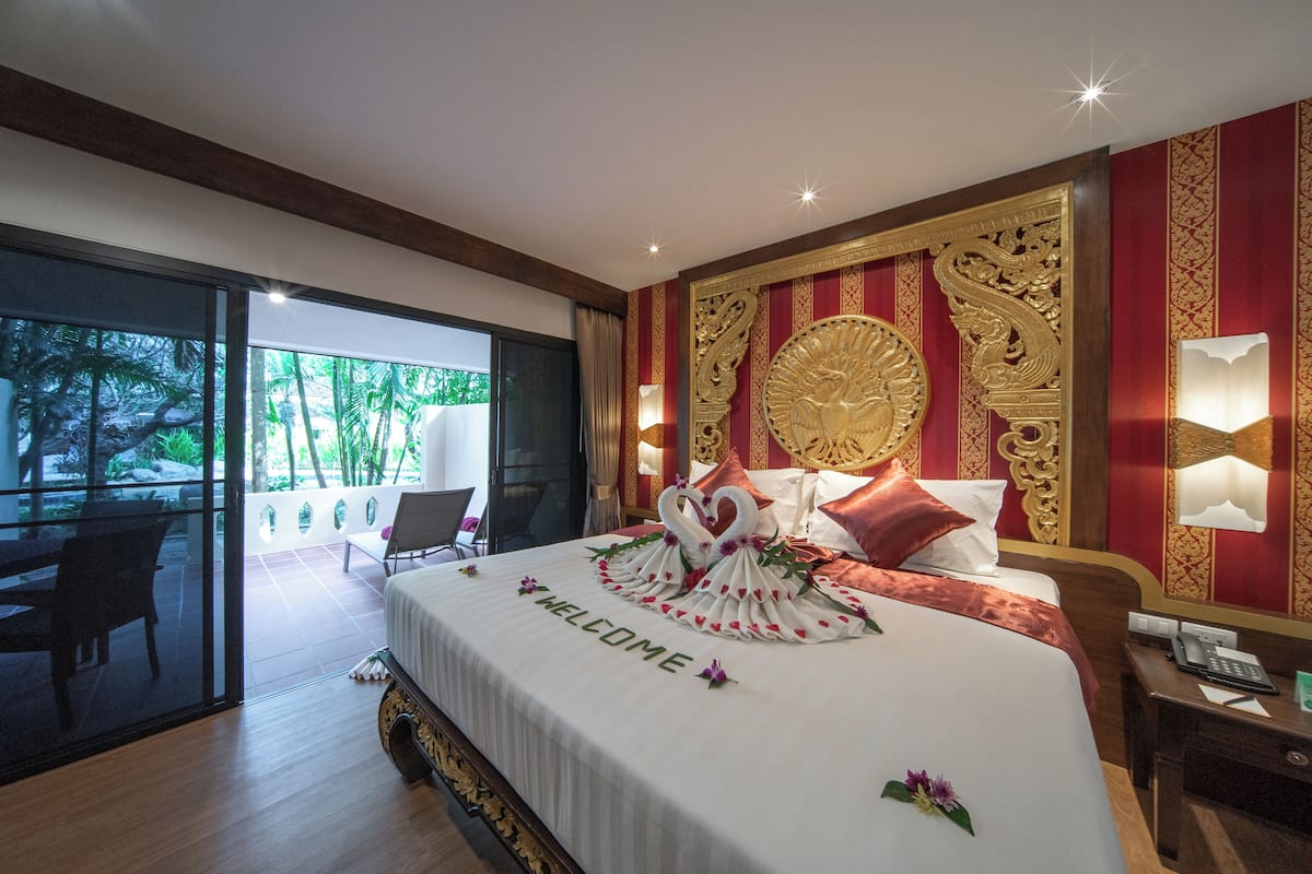 Habitación de hotel con cama, mesita de noche, escritorio y vistas a un jardín a través de una puerta de cristal.