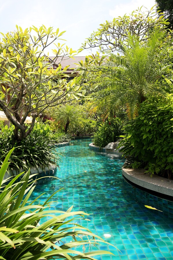 A swimming pool surrounded by lush greenery and a building in the background.