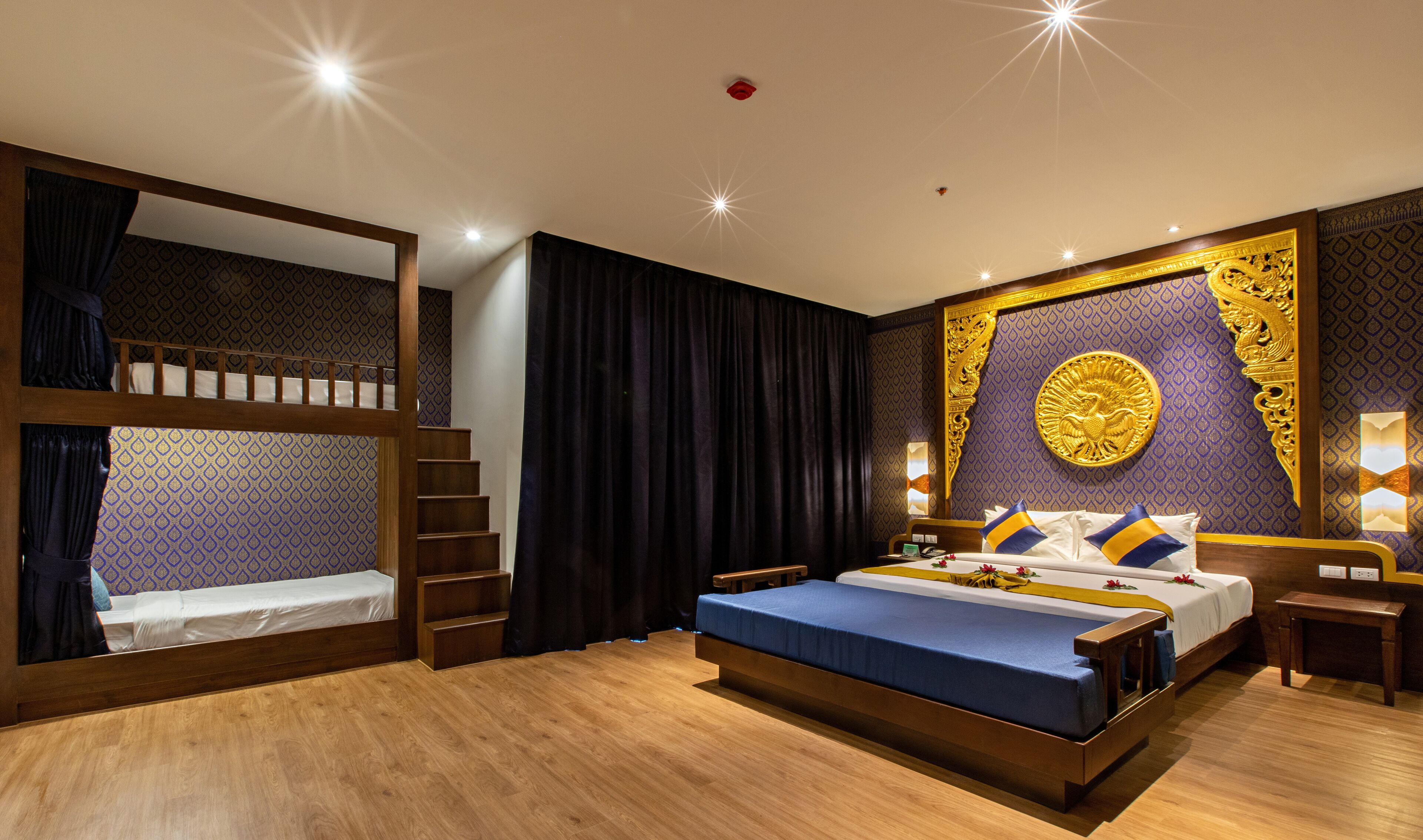 A hotel room with a bunk bed, a large bed with decorative pillows, a wooden floor, and a wall with a golden emblem.