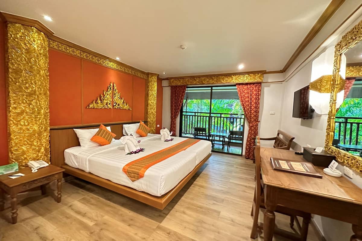 A hotel room with a large bed, a desk, a chair, a TV, and a balcony with a view of greenery.