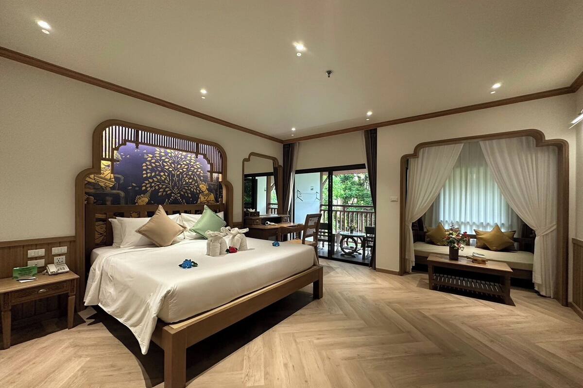 A spacious bedroom with a large bed, a wooden headboard, a desk, and a balcony with a view.