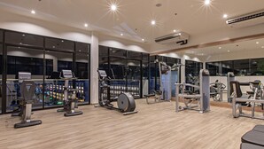 A modern gym with various exercise equipment, large windows, and a view of the city at night.