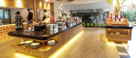 Un moderno vestíbulo de hotel con un mostrador central, estatuas decorativas y un fondo de pared de piedra.