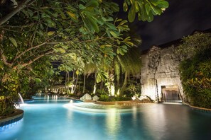 A nighttime swimming pool with a waterfall, surrounded by lush greenery and a stone wall. - Kata Palm Resort (Karon)