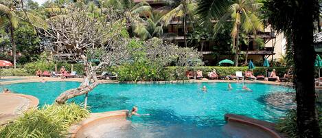 A pool area with multiple lounge chairs and umbrellas, surrounded by palm trees and greenery.