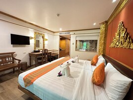 A hotel room with a large bed, a desk, a chair, a television, and a window with a view of greenery.