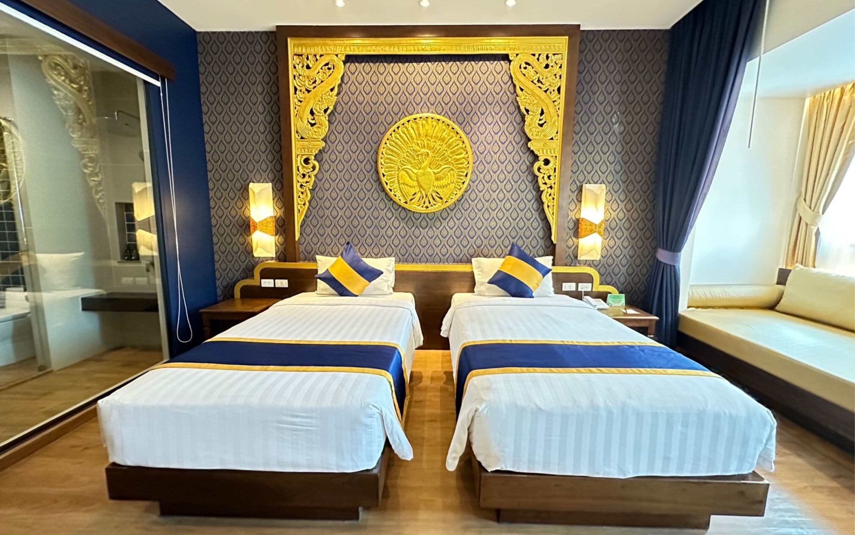 Habitación de hotel con dos camas, un sofá, una pared decorativa y un ventanal con cortinas.